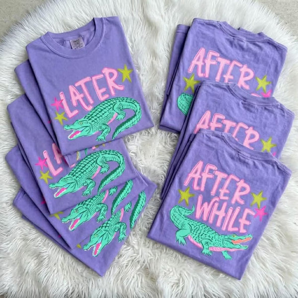 Purple t-shirts with alligator graphics and text on a white fluffy surface
