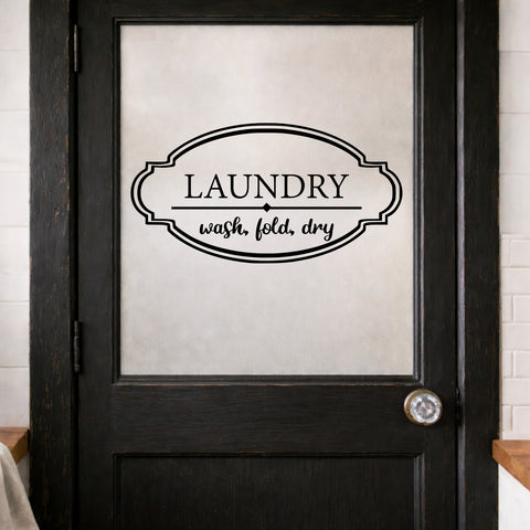 Black door with 'LAUNDRY wash, fold, dry' decal sign on a white brick wall background