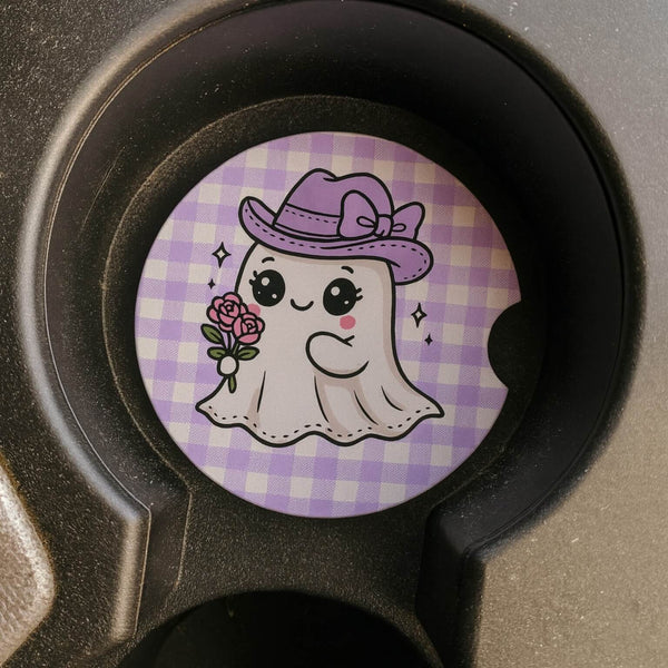 Cartoon car coaster with ghost wearing purple hat and flowers on a checkered background in a car cup holder.