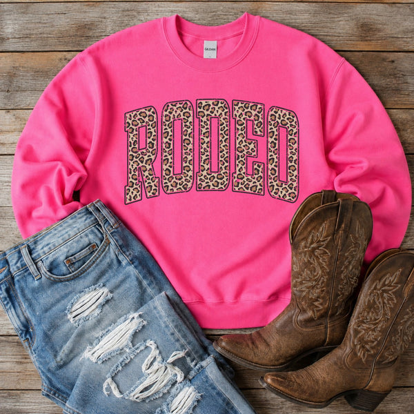 Hot pink Rodeo sweatshirt with leopard print lettering styled with ripped jeans and brown cowboy boots