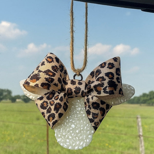 Leopard print bow car air freshener  a white polka dot background with a field and blue sky in the background