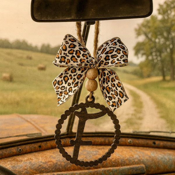 Leopard print bow car accessory on a vintage car's rearview mirror with a scenic background.