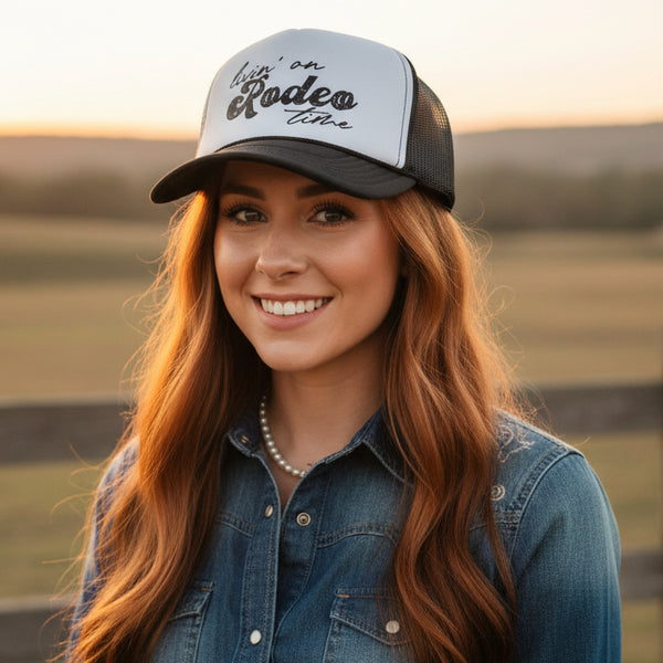Woman wearing a cap with 'Livin' on Rodeo Time' text, standing in a field.