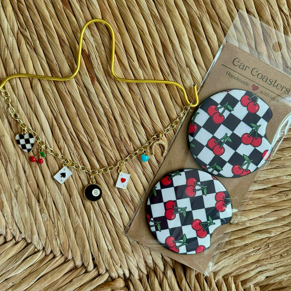 Two checkered car coasters with cherries on a wicker surface next to a gold car charm chain for rear view mirror