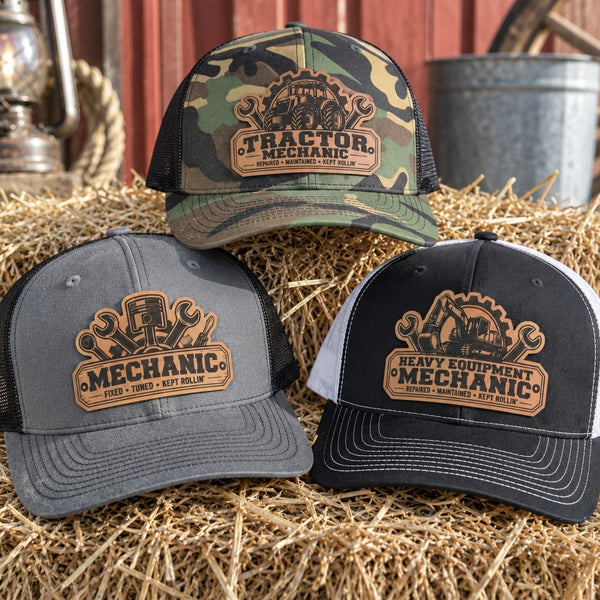 Tractor mechanic, automotive mechanic and heavy equipment mechanic leather patch trucker hats displayed together on hay