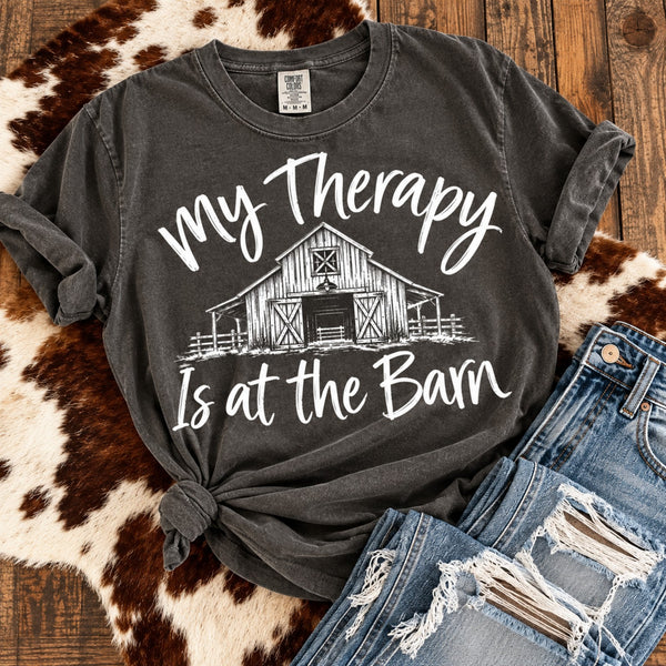 Pepper Comfort Colors farm life graphic tee featuring My Therapy Is at the Barn in white, styled with a side knot, ripped denim jeans and rustic cowhide.