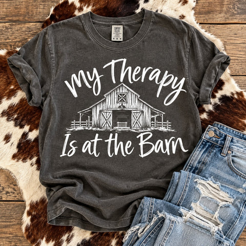 My Therapy Is at the Barn Comfort Colors Pepper graphic tee with white rustic barn design, distressed denim jeans and cowhide on a weathered wood background.