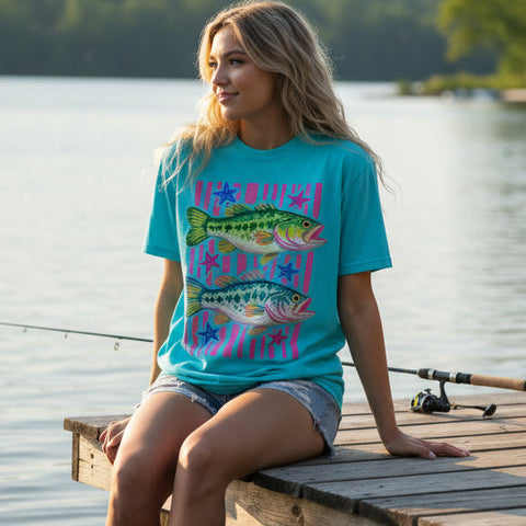 Woman wearing turquoise t-shirt with colorful fish graphic sitting on a fishing dock