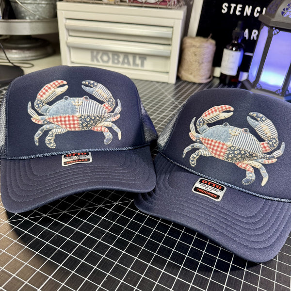 Two navy blue caps with crab designs on a checkered surface