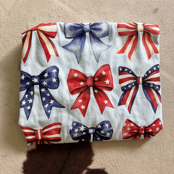 Patriotic bows graphic tee featuring red white and blue ribbon bows with stars and stripes on light blue shirt