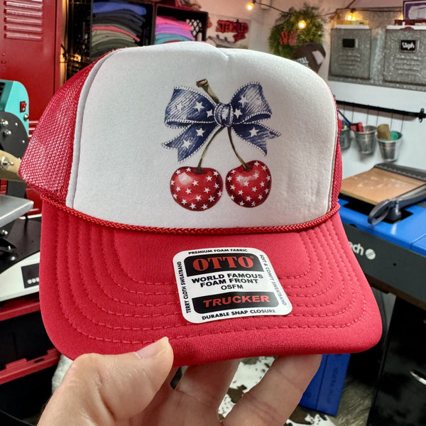 Patriotic cherries trucker hat featuring red star print cherries and blue bow on red and white foam mesh cap