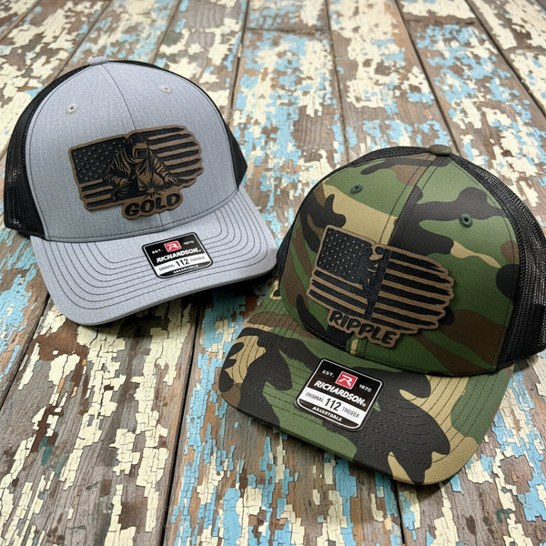 Gray and camo Richardson 112 hats with leather Blue Collar Tradesmen USA flag patches displayed on rustic wood. 
