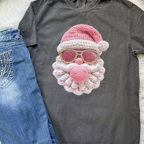Gray t-shirt with a pink and white crochet Santa Claus design on a light wooden surface.
