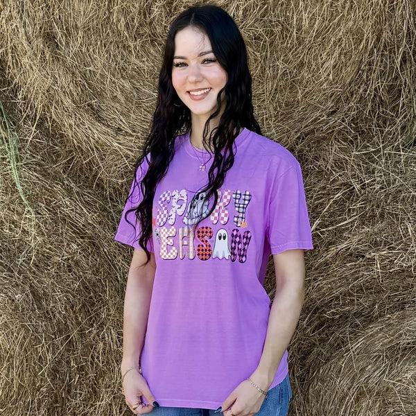 Woman wearing a purple 'Spooky Season' shirt standing in front of hay bales.