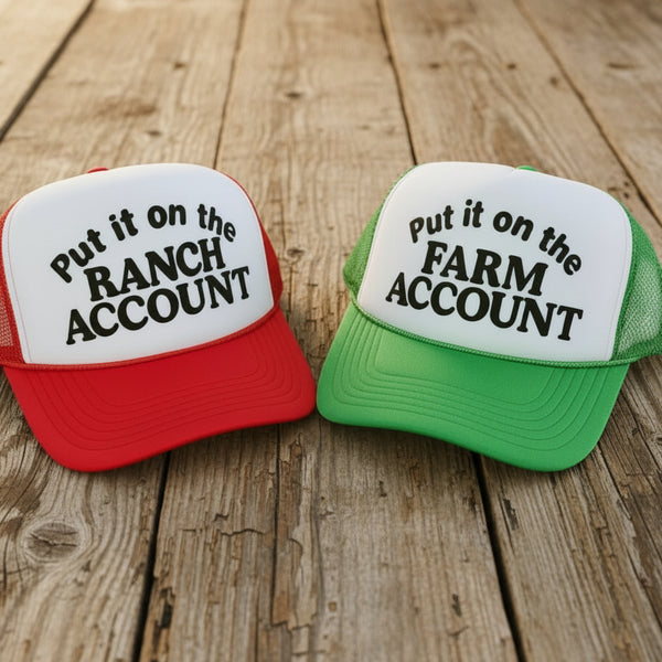 Red and green “Put it on the Ranch Account” and “Put it on the Farm Account” funny trucker hats on a rustic wooden surface – The Stenciled Barn