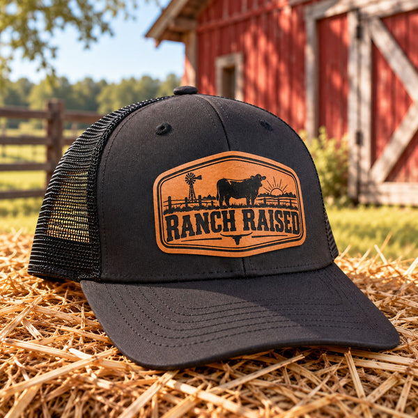 Ranch Raised youth trucker hat with cattle leather patch on hay by a red barn