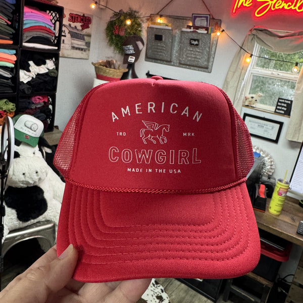 Red cap with 'American Cowgirl' text held in a casual indoor setting.