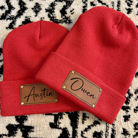 Two red beanies with name patches on a patterned surface