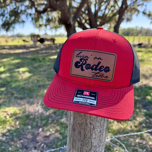 Living on Rodeo Time Leather Patch Richardson Trucker Hat sitting on a fence post with a cows in the background
