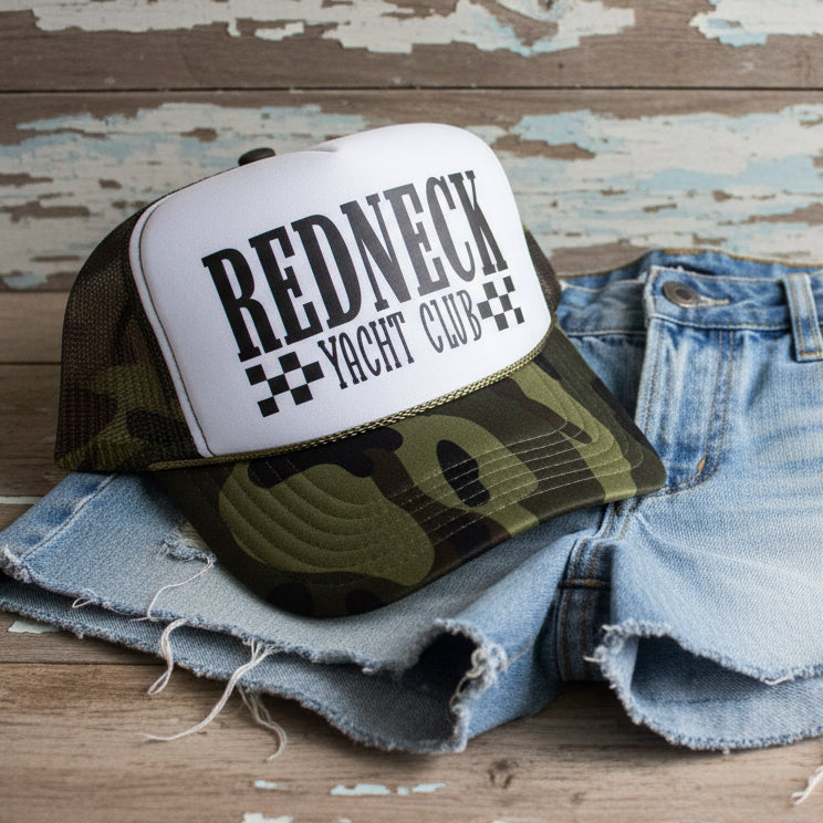 Redneck Yacht Club camo trucker hat with mesh back and southern country design on a wooden surface