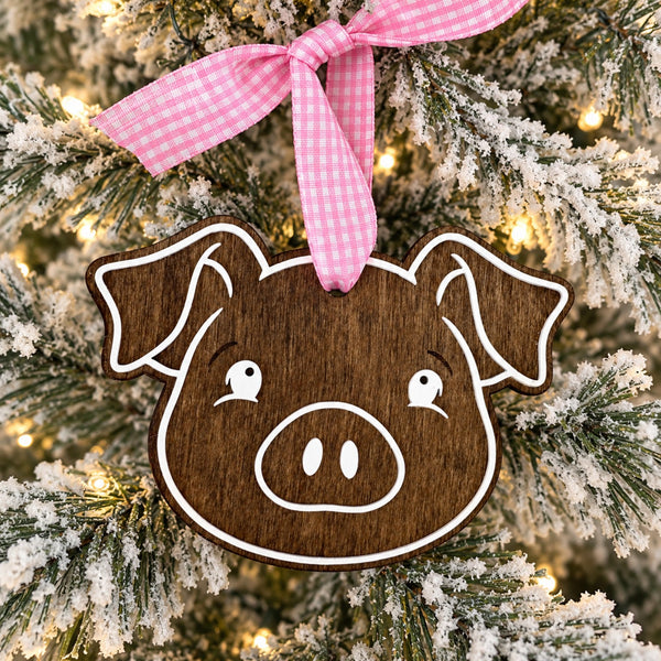 Rustic wooden pig Christmas ornament hanging on a flocked Christmas tree with pink gingham ribbon