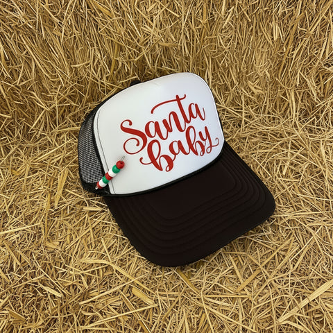 Trucker hat with 'Santa baby' text and beaded pin on a barn hay surface