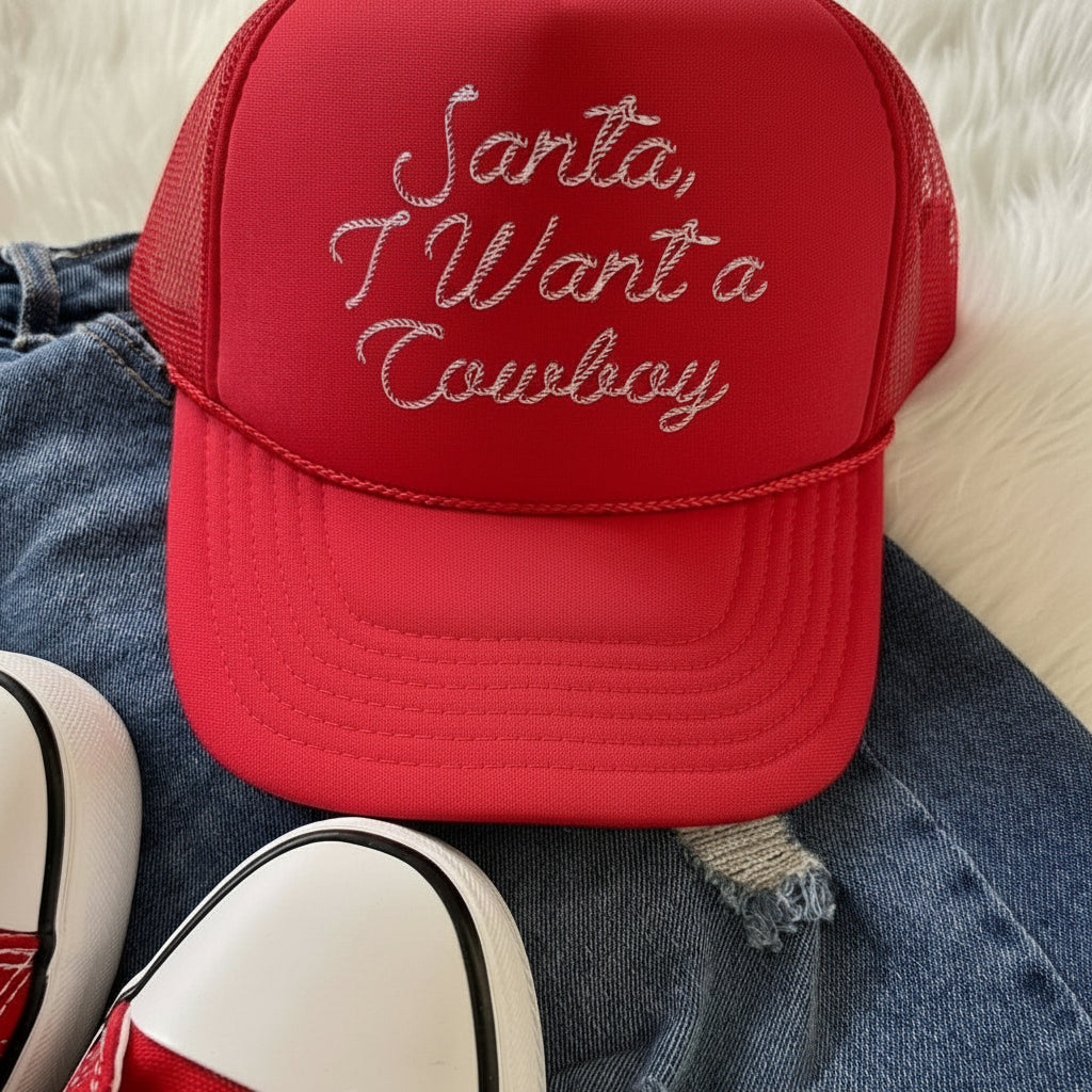 Red trucker hat with 'Santa, I Want a Cowboy' text on denim fabric.