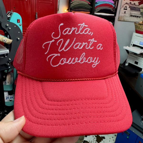 Santa I Want a Cowboy Christmas trucker hat with white script lettering on red foam mesh cap