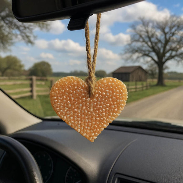 Heart-shaped car air freshener hanging from a car's rearview mirror with a scenic view outside.