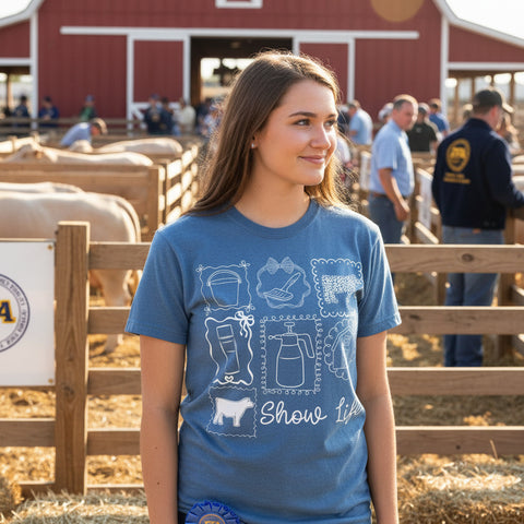 Young woman wearing Show Life coquette graphic tee with livestock show icons on blue Comfort Colors shirt at a county fair