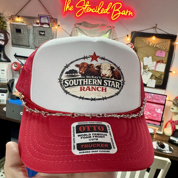 Red and white cap with 'Southern Star Ranch' logo held in front of a neon sign and store interior.
