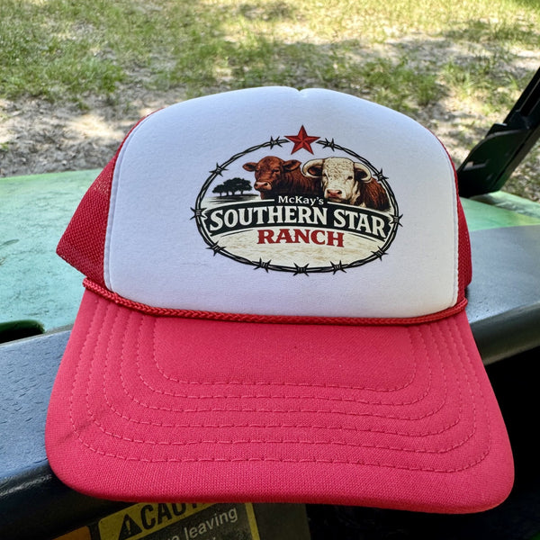 A red and white custom trucker hat featuring a 'McKay's Southern Star Ranch' logo on the front, resting on a green vehicle outdoors.