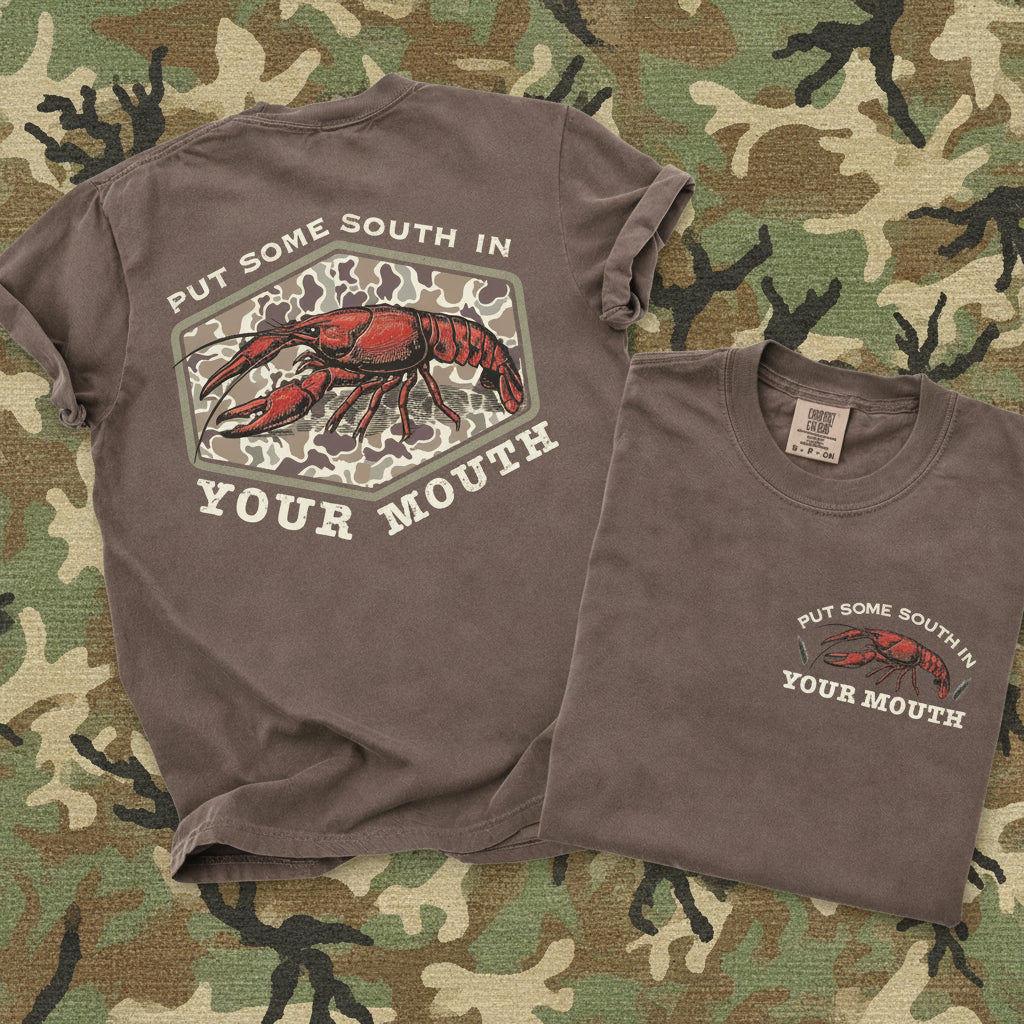 Brown Comfort Colors southern crawfish graphic tee with vintage camo design and “Put Some South In Your Mouth” slogan shown front and back on camo background