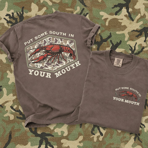 Brown Comfort Colors southern crawfish graphic tee with vintage camo design and “Put Some South In Your Mouth” slogan shown front and back on camo background
