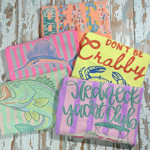Pastel Southern Country Graphic Tees Bundle Featuring Beach, Fishing & Lake Life Designs on Bright Comfort Colors Shirts – Sailfish Tee, Don’t Be Crabby Shirt, Bass Fish Graphic Tee & Redneck Yacht Club Tee Flat Lay Mockup