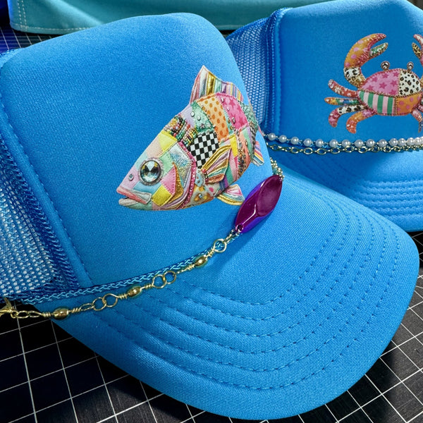 Closeup of neon blue summer fishing trucker hat with colorful patchwork fish graphic and handmade fishing lure hat chain in Southern coastal style