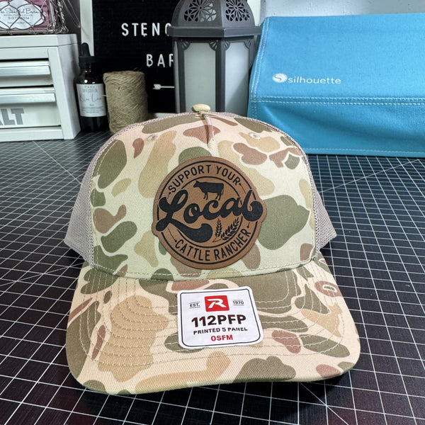 Camo Richardson 112 trucker hat with brown leather Support Your Local Cattle Rancher patch and tan mesh back.