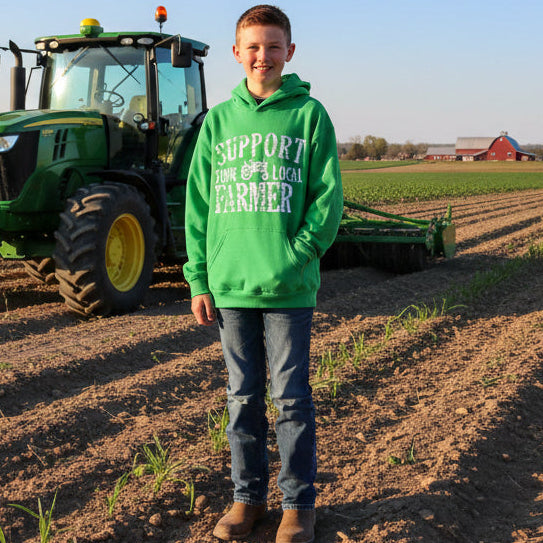 Boy wearing green hoodie with 'Support Your Local Farmer' text standing by a tractor