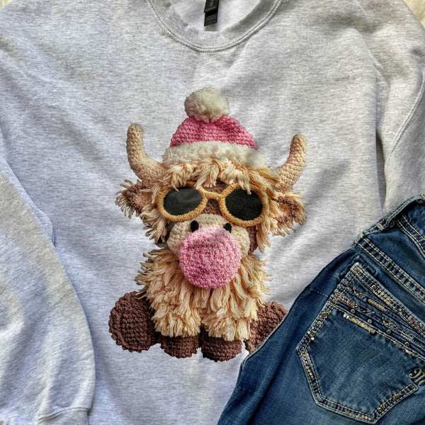 Gray sweatshirt with a cartoon cow wearing sunglasses and a pink hat, paired with blue jeans.