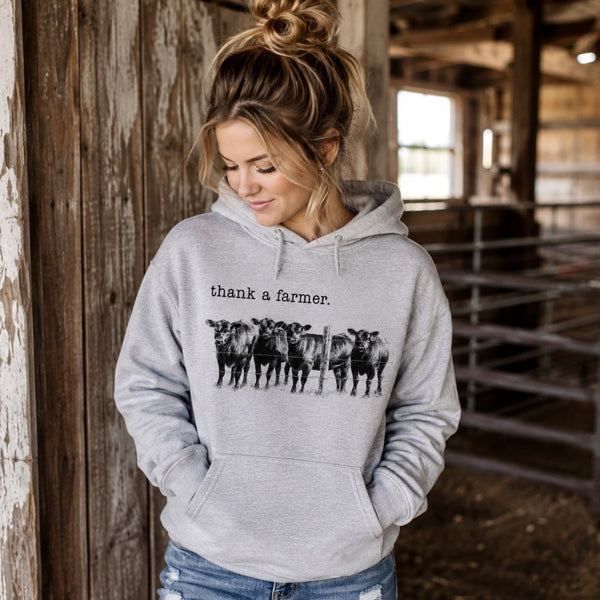 Woman wearing ash gray Thank a Farmer cattle hoodie inside a rustic barn