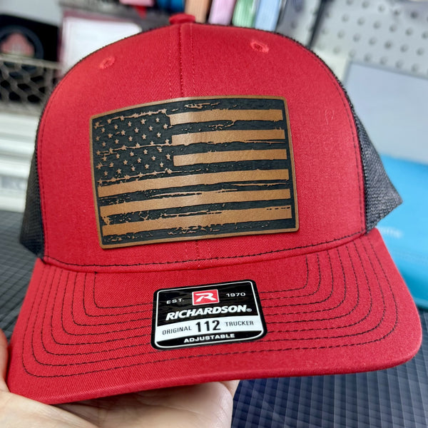 Red cap with American flag patch held by a hand against a blurred background