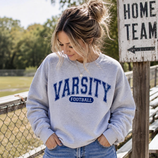 Woman wearing ash gray Varsity Football crewneck sweatshirt at an outdoor football field