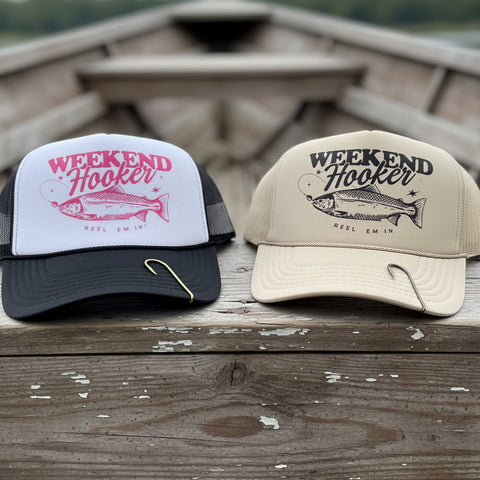 Two Weekend Hooker fishing trucker hats with vintage fish graphics and decorative fishing hook hat clips in black and cream color options