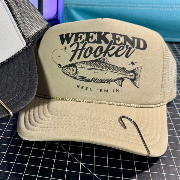 Beige cap with 'Weekend Hooker' fishing graphic on a grid background