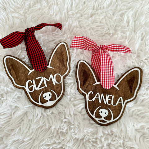 Two wooden dog-shaped ornaments with names 'Gizmo' and 'Canela' on a fluffy white surface.