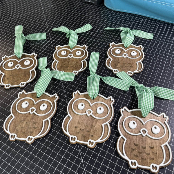 Wooden owl ornaments with green ribbons on a grid surface