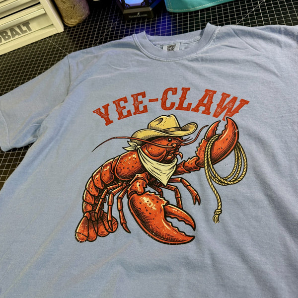 Blue t-shirt with a lobster graphic and 'YEE-CLAW' text on a checkered surface.