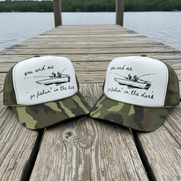 Two green and white caps with a fishing design on a wooden dock by a lake.