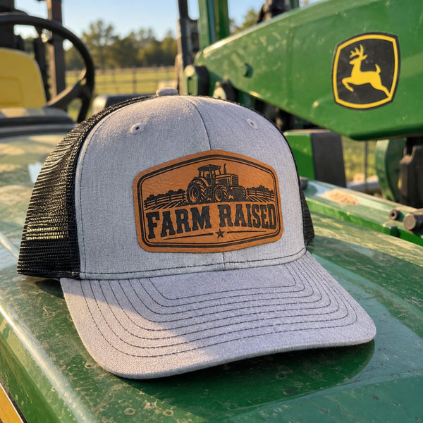 Youth Farm Raised tractor Richardson trucker hat with engraved leather patch displayed on green farm tractor