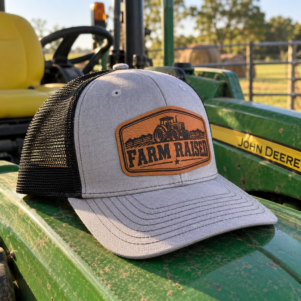 Gray and black youth Farm Raised tractor patch hat displayed on green John Deere tractor
